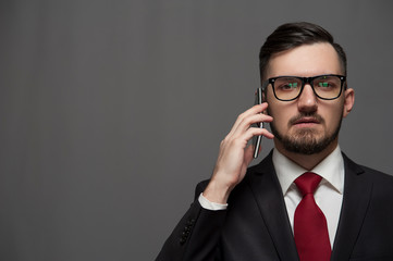 Close-up - Serious young businessman in formal suit talking to someone on smartphone on gray background. Place for text