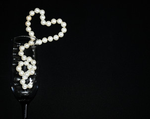 Wine glass. Decoration of white pearls on black background. Heart-shaped decoration.  Valentine's day layout. Declaration of love.