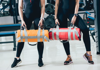Athletic young women training with sandbags at gray background. Crossfit center