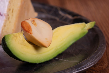 Avocado on black plate. Sliced avocado top view on black wooden background ripe green brown alligator pear two halves with a seed. Green leafs. Professional photo studio of kitchen