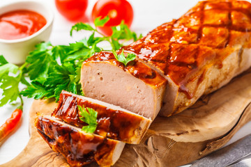 Baked meatloaf with greens and barbecue sauce on a wooden board, white background.