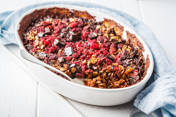 Baked oatmeal with berries and chocolate in a white dish.