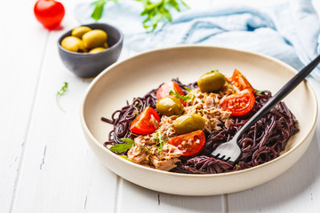 Black rice pasta with tuna, tomatoes and olives in a white plate.