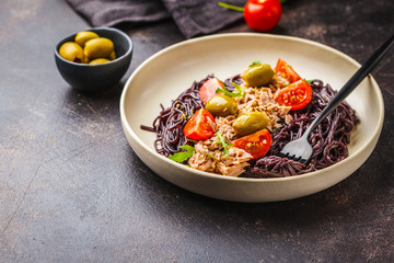 Black rice pasta with tuna, tomatoes and olives in a white plate.