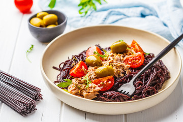 Black rice pasta with tuna, tomatoes and olives in a white plate.