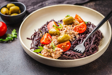 Black rice pasta with tuna, tomatoes and olives in a white plate.
