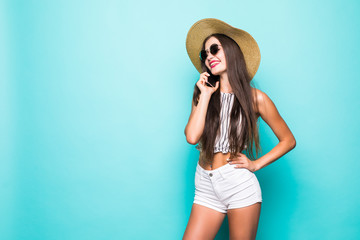 Beautiful laughing woman in summer hat and sunglasses talking on mobile phone on blue background