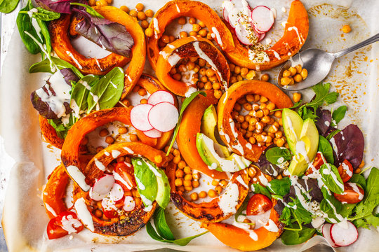 Baked pumpkin with chickpeas on a baking sheet with avocado, tahini and vegetables.