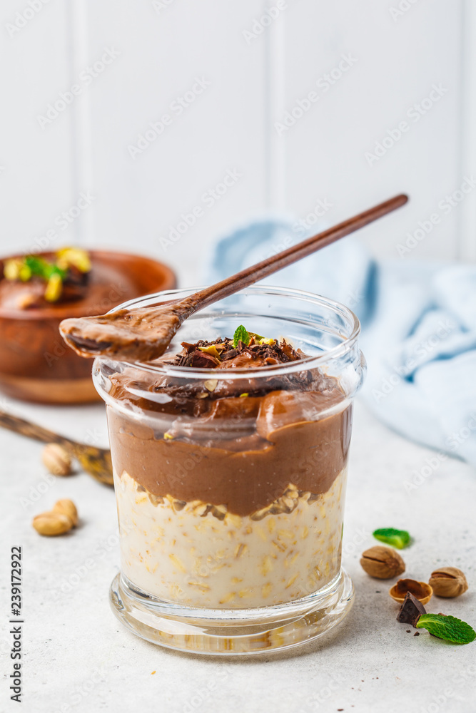 Wall mural Overnight oatmeal with milk and chocolate mousse in glass on a white background.