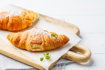 Fresh croissants on white wooden background.