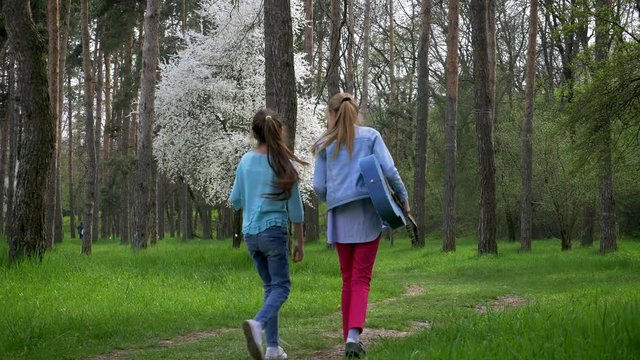children walk in the Park. Little girlfriends are walking in nature with acoustic guitar . beautiful forest path, juvenile girl outgoing in the distance. emotions and joy