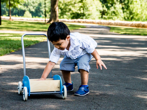 Latino Child Playing Outside In A Park With Toys And Trees In The Background