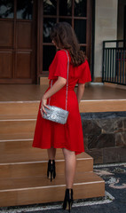 Obraz na płótnie Canvas Fashion women accessories. Fashionable woman in red dress with luxury snakeskin python handbag outside. Snakeskin fashion concept. Model near the expensive villa. Girl rises in her villa