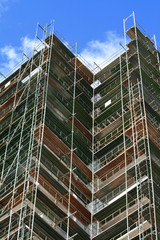 Part of a building covered by a steel scaffolding in front of the blue sky