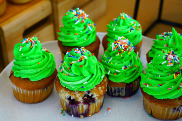 Platter of blueberry cupcakes with green buttercream frosting and colorful sprinkles like a Christmas tree