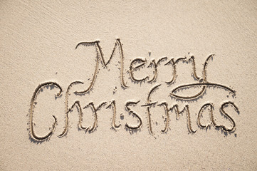 Merry Christmas message handwritten in textured calligraphy letters on smooth sand background