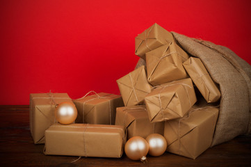 Christmas presents wrapped in ecological paper in a gift sack on a wooden table with christmas balls