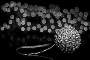 A shiny silver ball from a Christmas tree lying on a table on the background of gerlyani with beautiful bokeh. Black and white.