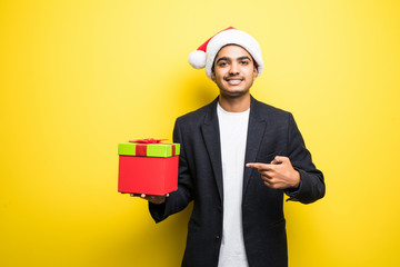 Smiling indian man in Santa Hat Pointing at Big Gift Box isolated on yellow background