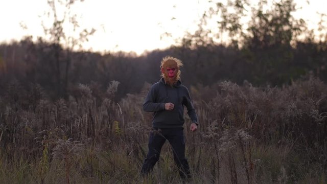 General plan. In the autumn field a guy dancing in a mask of a monkey 4K Slow Mo