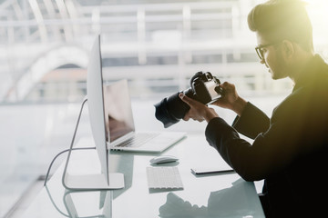 Young cheerful photographer man use photocamera while working in his office