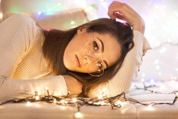 Young woman with glasses lying down and there are christmas lights around her