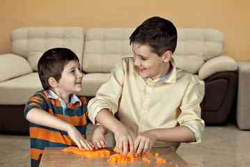 Two boys are playing with plasticine at the table. Children mold sculptures of kinetic sand. Figure...