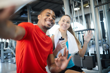 Happy girl and guy in activewear posing for selfie in fitness center during break between workouts
