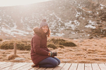 Fototapeta na wymiar young woman photographer taking photo at mountain peak and smiling at sunset