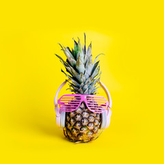 Fashionable  trendy pineapple fruit with headphones and sun glasses listen to the music over bright pastel yellow background.