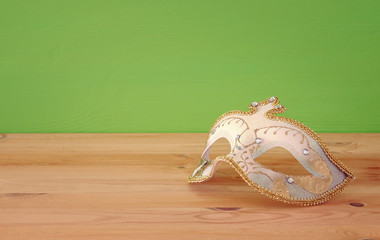 carnival party celebration concept with elegant gold mask over wooden table and green background background.