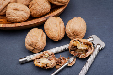 Brown premium raw organic walnuts and nutcracker in wooden bowl on natural stone background