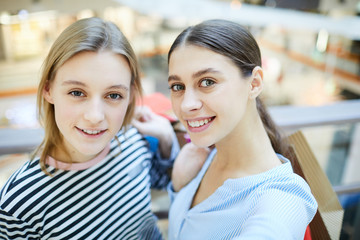 Two young cheerful shoppers standing in front of camera during seasonal sale in the mall