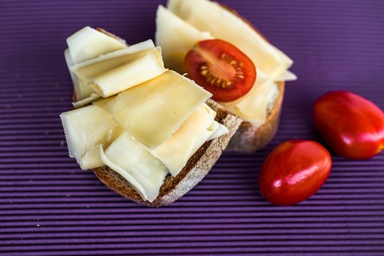Bread with sliced cheese and tomato on violet background.