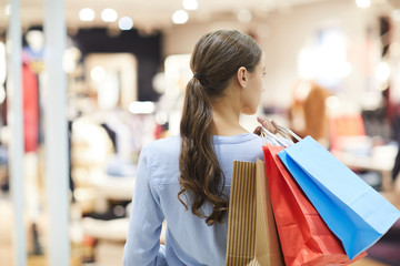 Rear view of young shopper with ponytail looking around while hanging in large mall at seasonal sale