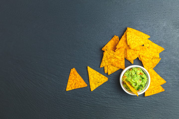 Guacamole and nachos with ingredients on the background of a black stone board