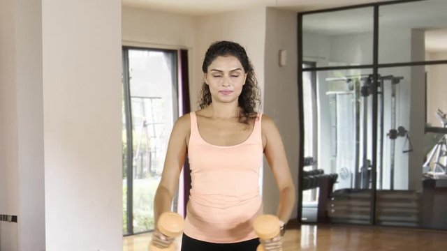 Attractive Asian woman exercising in fitness center with two dumbbells and smiling at the camera. Shot in 4k resolution
