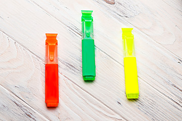 wooden background painted white. on it are three colors marker yellow green pink