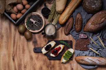 Breakfast and baked bread concept. Fresh fragrant bread and egg on wooden table. Fresh bread and coffee and wheat on wood black background. Sesame seeds in the dish. Coffee in cup.