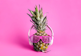 Fashionable  trendy pineapple fruit with headphones and sun glasses listen to the music over bright pastel pink background.