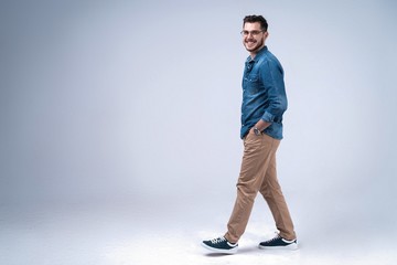 side view of a smiling young casual man walking , on gray background. - Powered by Adobe