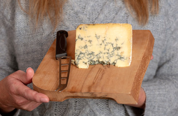 Slice of blue cheese on a wooden cheese board with a cheese knife