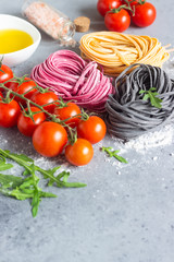 Ingredient of traditional mediterranean cuisine. Raw colored pasta noodle, olive oil, tomatoes and arugula. Copy space for text. Food background.