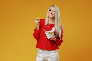 Bright blond woman eating asian fast food from takeaway box with chop sticks, Wok noodles concept