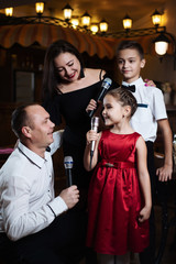 Little girl sings into a microphone in a circle of a happy family.