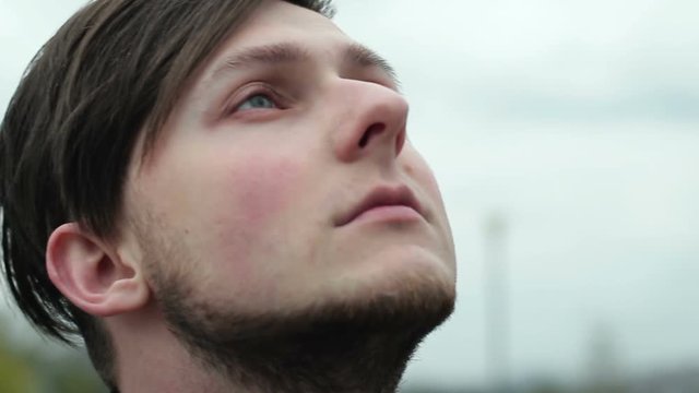 Serious young man looks into the sky in cloudy weather