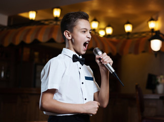 Boy in a white shirt singing into the microphone in a restaurant. baby karaoke.