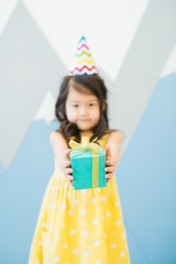 Happy birthday to you: cute Asian girl in yellow dress standing against creative drawn wall and giving small gift box to camera