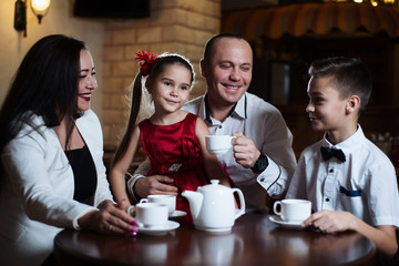 Family came together in a cafe. Mom, dad, little daughter and son drink tea. They are happy together. Happy family lunch concept.