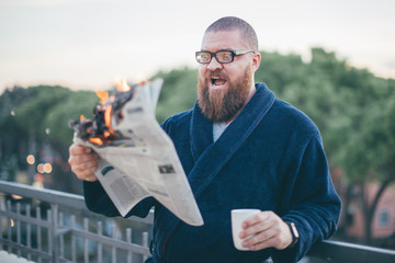 Portrait of excited (shocked) bearded man looking to the newspaper (on fire) - burning magazine in...